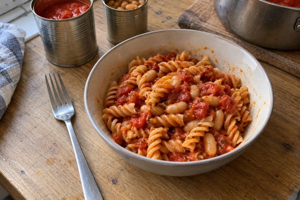 A bowl of pasta with tomato and white bean sauce on a wooden kitchen table.