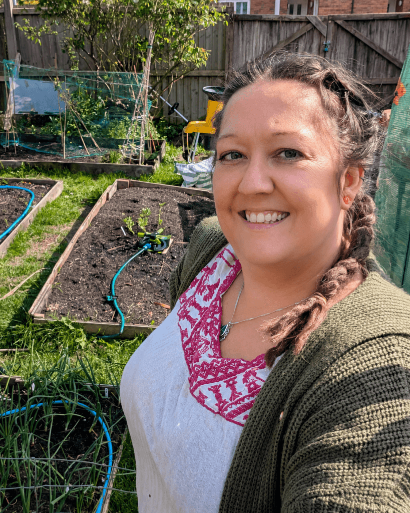 Niki in a green cardigan beside the garden beds